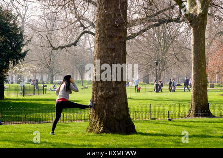 A woman doing stretches in St James's Park London while talking on her mobile phone Stock Photo