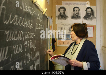 Podol village, Tver region, Russia - May 5, 2006: School teacher writes with chalk on the blackboard in the classroom of rural school. Stock Photo