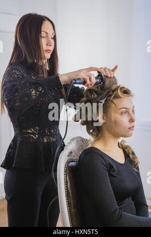 Professional hairdresser, stylist making curls in white make up room. Beauty and haircare concept Stock Photo