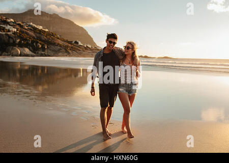 Full length portrait of romantic young couple walking on sea shore. Man and woman enjoying a day at beach. Stock Photo