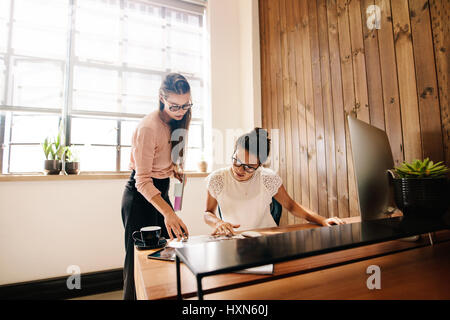 Two business women reading documents on desk. Colleagues working together in modern office. Stock Photo