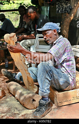 Namanga, Tanzania - February 9, 2008: Dark skinned middle-aged African, master wood carving works of art workshop, under the open sky. Art workshop ou Stock Photo