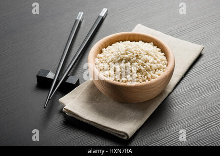 wooden bowl with rice and japanese chopsticks on black wooden table Stock Photo
