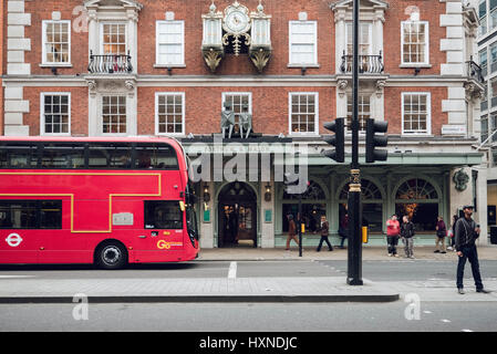 A red London bus and pedestrians outside Fortnum & Mason's luxury store on Piccadilly, London. Stock Photo