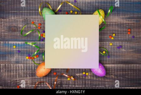 Colored Easter eggs, confetti and festive ribbons are scattered on a wooden background. In the center there is a place for text. Easter image. Stock Photo