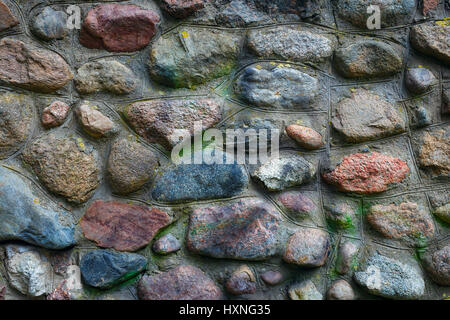 Background from part of the wall of stones. Stones of different colors and shapes. In some places the wall has moss and traces of paint that gives it  Stock Photo
