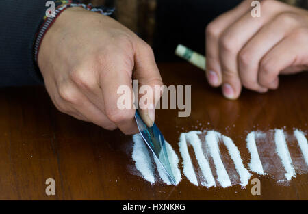 Mans hands preparing lines of white cocaine powder on desk using credit card, rolled up twenty dollar bill in other hand Stock Photo