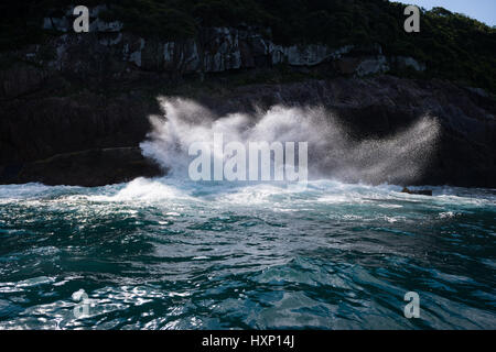 A wave crashes on the rocky cliffs of Ilhabela Stock Photo