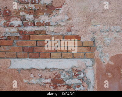 Old red brick wall in italy with many repairs, cement and plaster and signs of damage Stock Photo