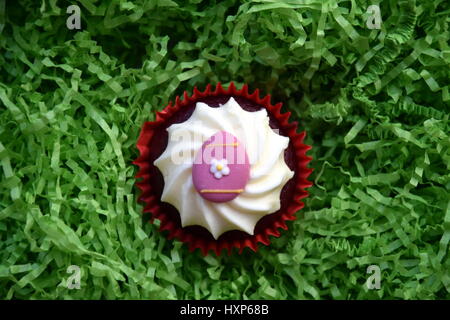 Home made easter muffin decorated with easter egg. Easter concept, pink egg on top of the red and white cupcake in green nest. Stock Photo