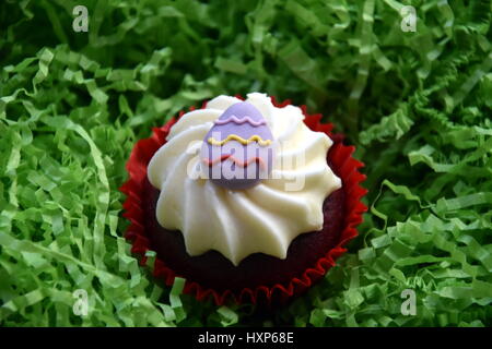 Home made easter muffins decorated with easter eggs. Easter concept, purple egg on top of the red and white cupcake in green nest. Stock Photo