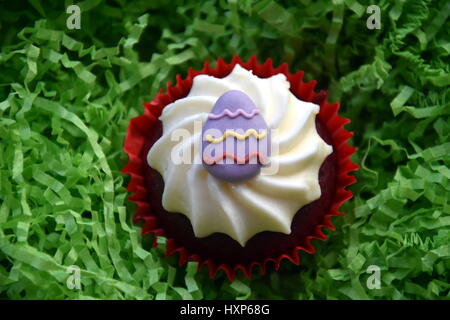 Home made easter muffins decorated with easter eggs. Easter concept, purple egg on top of the red and white cupcake in green nest. Stock Photo