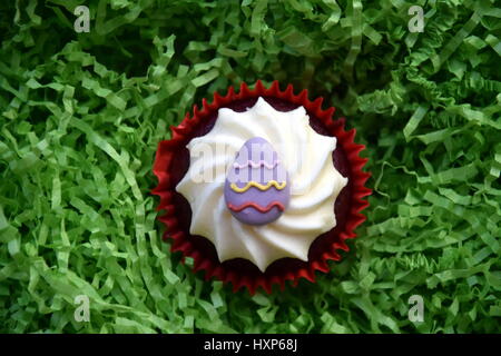 Home made easter muffins decorated with easter eggs. Easter concept, purple egg on top of the red and white cupcake in green nest. Stock Photo