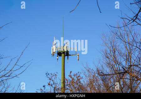 Steel telecommunication tower with antennas over blue sky and trees Stock Photo