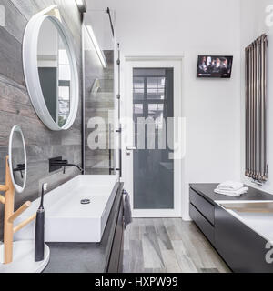 Spacious bathroom with elegant white washbasin and television above bathtub Stock Photo