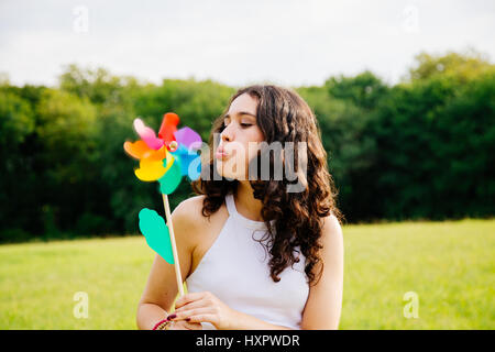 Beautiful young woman blowing a windmill toy in a green landscape Stock Photo