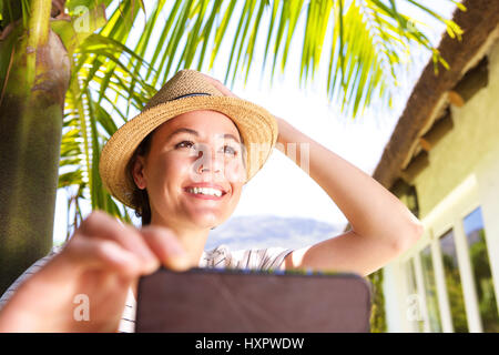 Close up portrait of beautiful young woman with hat standing in backyard taking selfie with cell phone Stock Photo