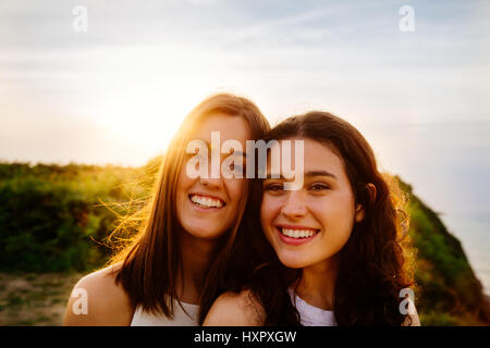 Portrait of two happy female friends on a cliff at sunset. Sun flare. Stock Photo