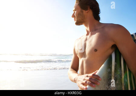 Portrait of a male surfer carrying surfboard at the beach Stock Photo