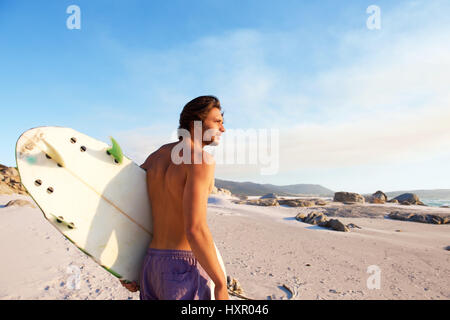 Portrait of handsome young man walking on beach with surfboard Stock Photo