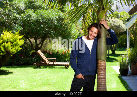 Portrait of attractive young man leaning against tree and smiling Stock Photo