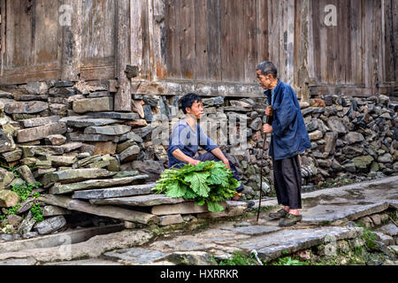 Zengchong Dong Village, Guizhou Province, China - April 11, 2010: Elderly and young farmers talking near wooden barn on a rural street. Stock Photo