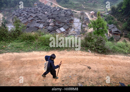 Zengchong Dong Village, Guizhou Province, China - April 11, 2010: An elderly Chinese woman walking back from field work, she goes on a mountain dirt r Stock Photo