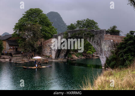 Yangshuo, Guangxi, China - March 31, 2010: Cruising on bamboo boat in Yulong River, Guilin, Dragon Bridge, rainy spring weather, picturesque tourist t Stock Photo