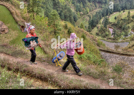 Langde Village, Guizhou, China - April 15, 2010: Two Asian women peasant farmers go to the field with the equipment for spraying plants. Stock Photo