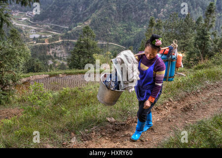 Langde Village, Guizhou, China - April 15, 2010: Chinese woman farmer peasant carries the weight on your shoulder. Asian female goes on a farm field w Stock Photo