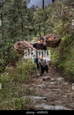 Langde Village, Guizhou, China - April 15, 2010: Chinese peasant farmer man carries the weight on your shoulder. Asian family farmer goes to work in   Stock Photo