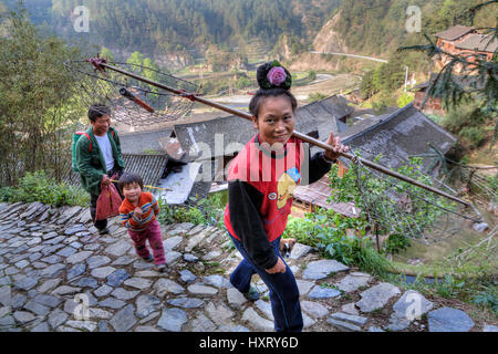 Langde Village, Guizhou, China - April 15, 2010: Woman farmer with a rose in her hair is on rural stoun road, Langde Miao Village. Stock Photo