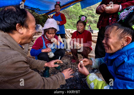 Langde Village, Guizhou, China - April 16, 2010: Chinese peasants, farmers, villagers, men and women sit around the fire, talking, eating and laughing Stock Photo