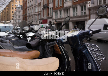 A row of Vespa scooters parked on a street in London, Mayfair after the rain. Many people have turned to motorcycles to avoid the congestion charge. Stock Photo