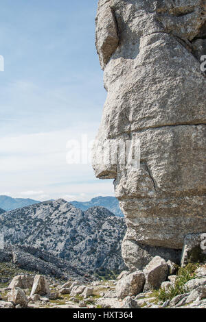 Close-up of red indian side face shape monolith grey rock against of beautiful endless mountain chain Stock Photo