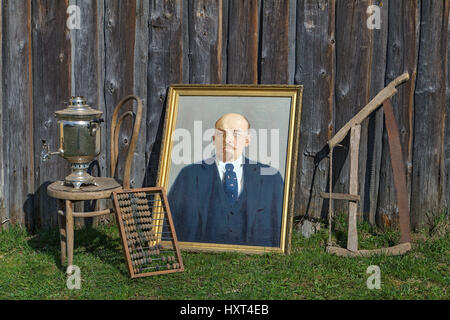 On the grass near the barn are obsolete things Russian peasants, rusty hand saw, wooden abacus, a samovar, the oil portrait of Vladimir Lenin on canva Stock Photo