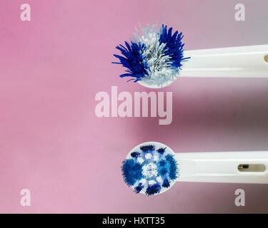 Close-up on the top of the head of a worn out and a new white and blue heads of an electric toothbrush against pink gradient Stock Photo