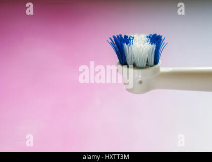Close-up on the side of the head of a worn out white and blue head of an electric toothbrush against pink gradient Stock Photo