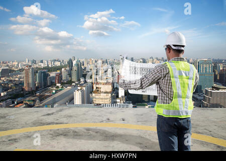 Construction engineer looking at blueprints for planning building project with cityscape background Stock Photo