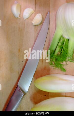 Kitchen knife and vegetables on a wooden cutting board in the kitchen, preparing and cutting the vegetables while cooking a healthy meal with garlic,  Stock Photo