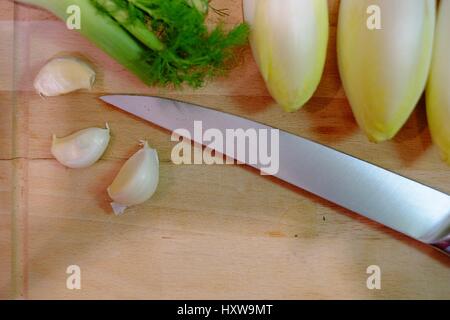 Kitchen knife and vegetables on a wooden cutting board in the kitchen, preparing and cutting the vegetables while cooking a healthy meal with garlic,  Stock Photo