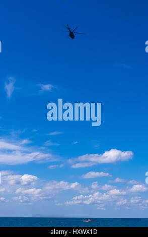 helicopter flying in the blue sky with white clouds over the sea Stock Photo