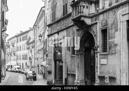 Trento, Italy - March 21, 2017: Houses with diverse facades in an alley in the old town. Cars are parked parallel. The picture is monochrome. Stock Photo