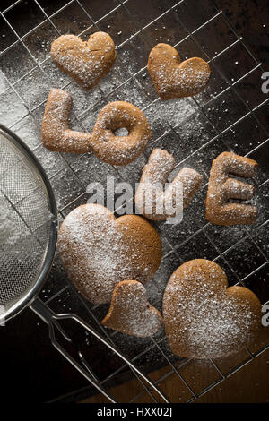 Freshly made gingerbread cookies after they have been dusted with icing sugar on a baking tray. Some are heart shaped and some spell out the word 'lov Stock Photo