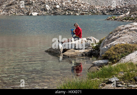CA03142-00...CALIFORNIA - John Muir Trail hiker using a squeeze bag to purify water at a small tarn above Lake Marjorie in Kings Canyon National Park. Stock Photo