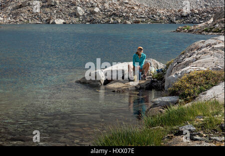 CA03143-00...CALIFORNIA - John Muir Trail hiker using a squeeze bag to purify water at a small tarn above Lake Marjorie in Kings Canyon National Park. Stock Photo