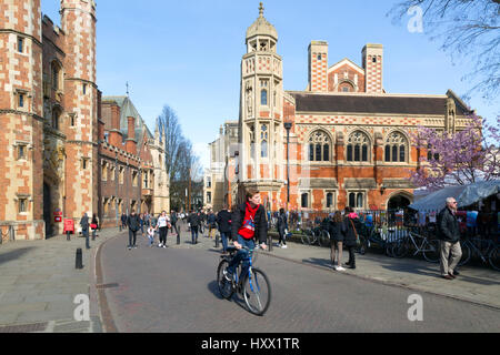 Cambridge university student cycling a bicycle past St Johns College; Trinity Street, Cambridge England Cambridge UK Stock Photo