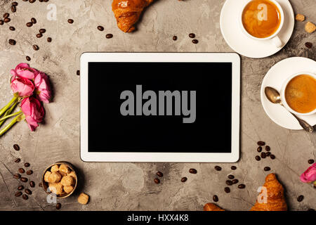 Tablet, coffee and croissants on grey stone background. Top view. Flat lay style. Stock Photo