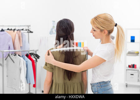 young dressmaker gets shoulders measures of client in the showroom Stock Photo