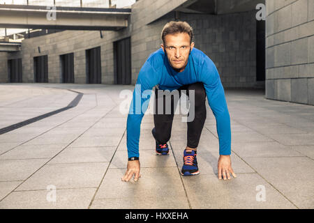 Handsome middle aged serious man in blue black sports uniform and headphones and fitness tracker is running in the city. Stock Photo